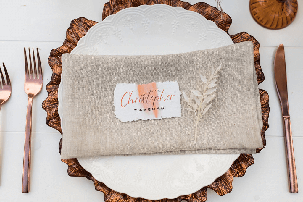 A place setting with rose gold utensils and a sprig of foliage