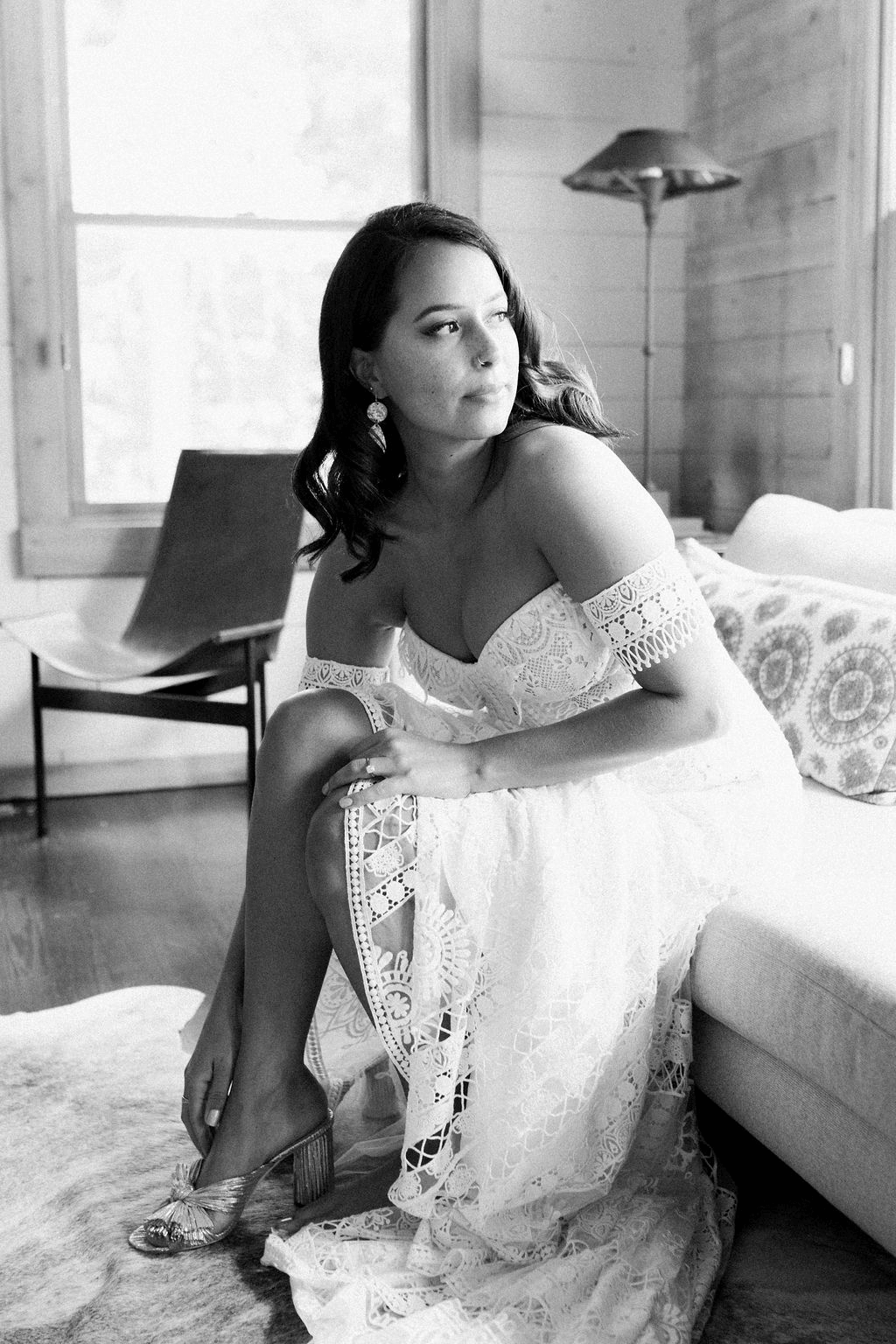 A bride in her wedding dress putting on her shoes while looking away